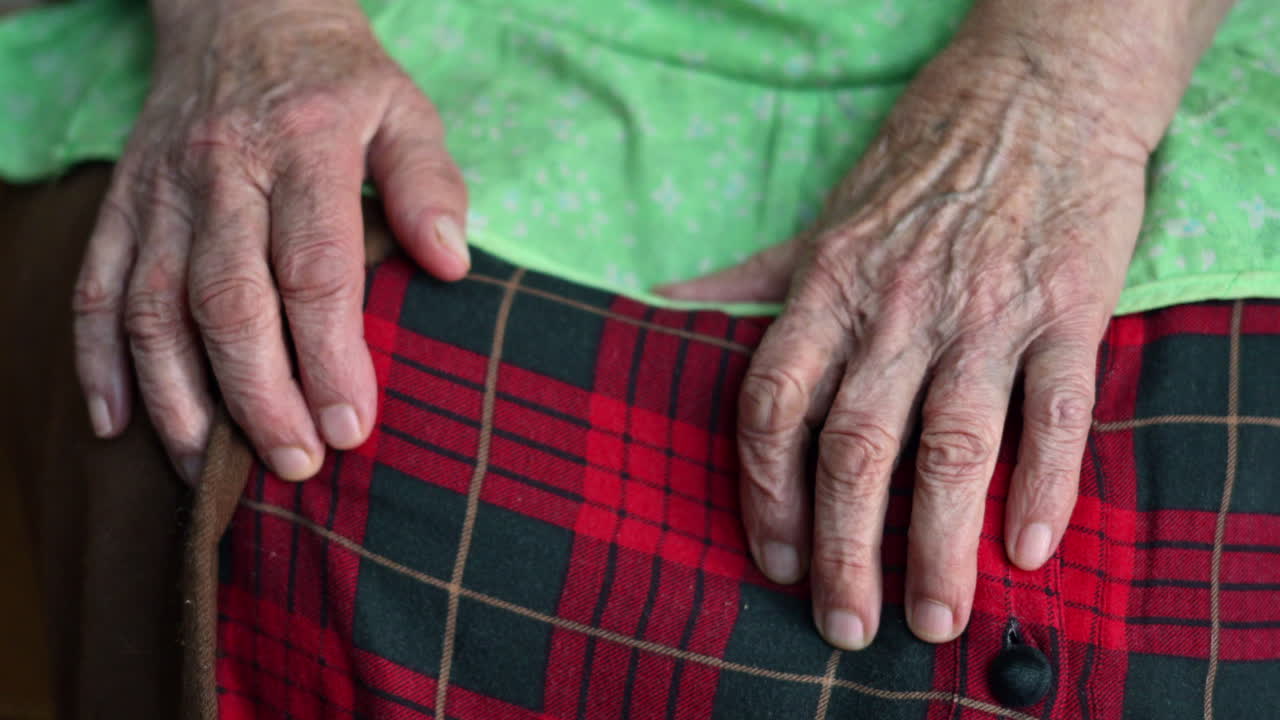Close up of the hands of an old woman sitting in a pleated, red skirt