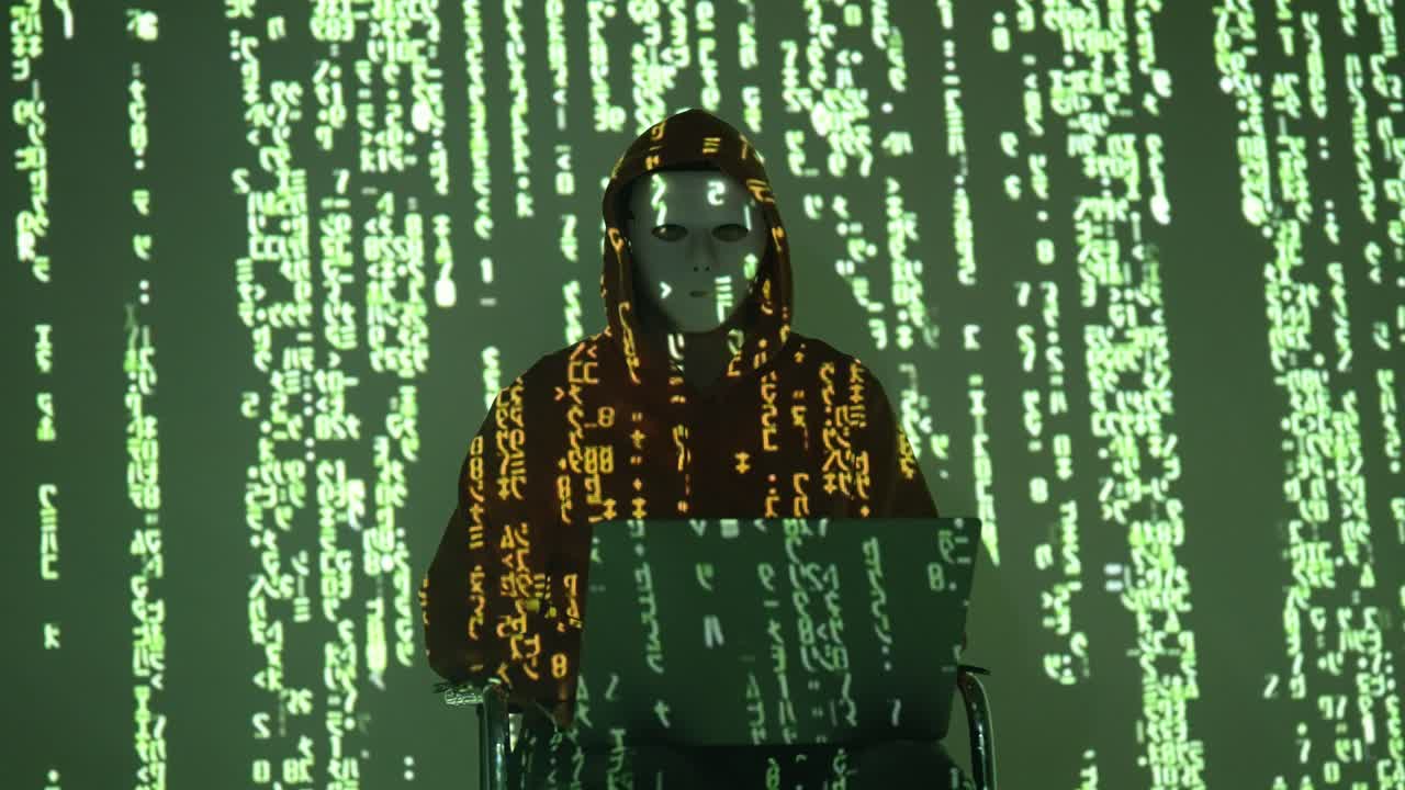 A hooded, masked hacker works on a laptop as green code rains across the background. This cyber-themed scene conveys secrecy, intrusion, and the hidden side of digital operations