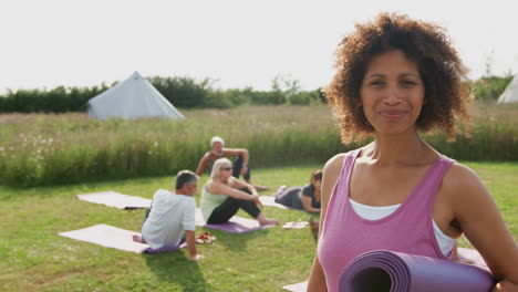 portrait of mature woman on outdoor yoga retreat with friends and campsite in background