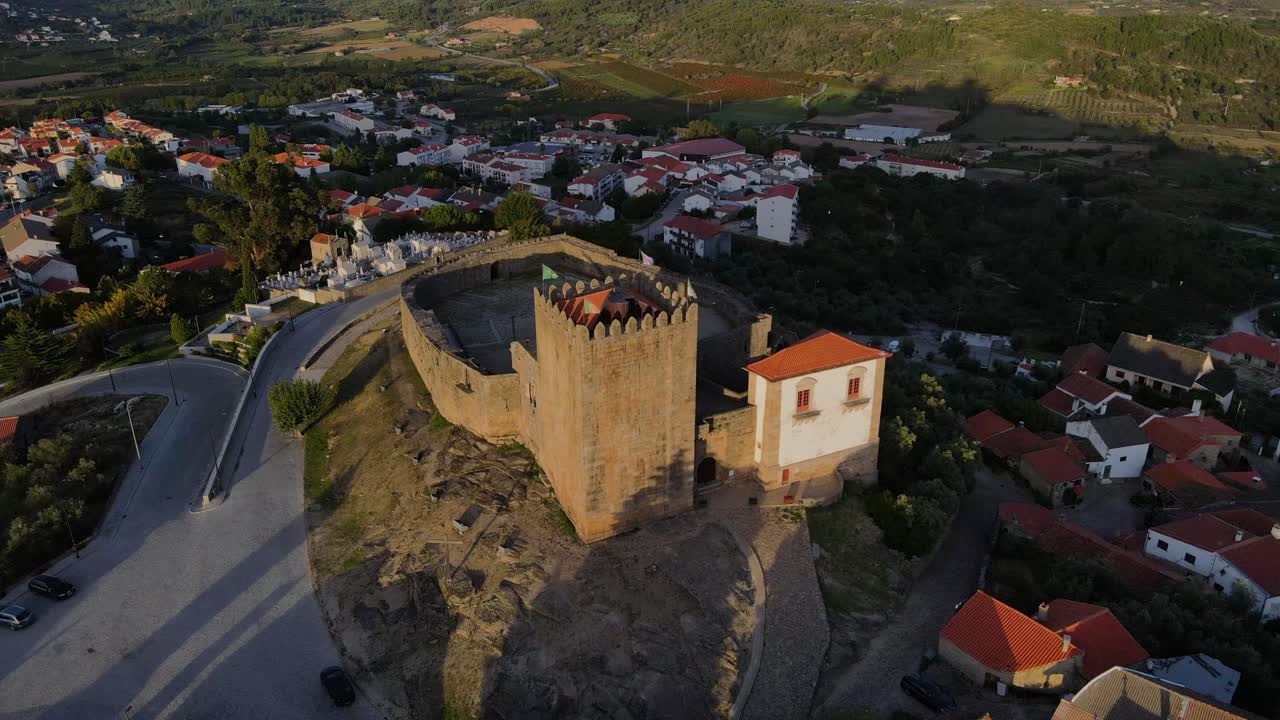 Un drone si allontana dalla torre del castello di Belmont al tramonto, circondato da uccelli.
