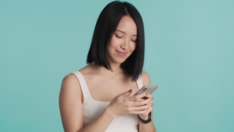 Asiatische-Frau-Schreibt-SMS-Auf-Dem-Smartphone-Und-Lächelt-In-Die-Kamera.