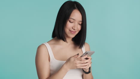 asian woman texting on smartphone and smiling at the camera.