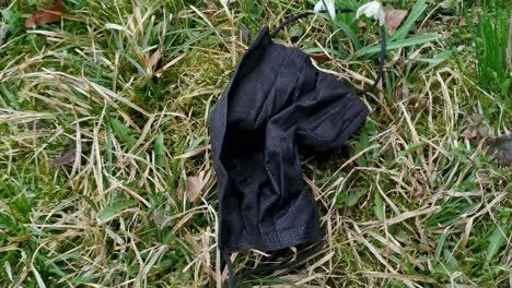 closeup of black surgical face mask on ground grass, pandemic pollution, handheld, day