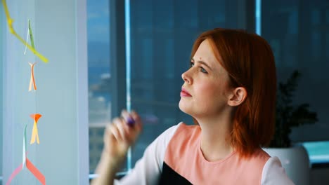 female executive writing over sticky note on glass board