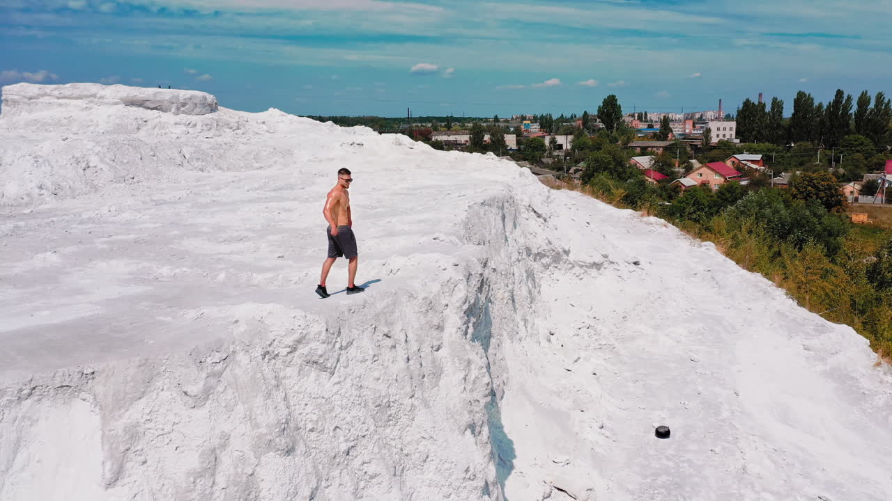 Brutal strong bodybuilder posing outdoor. Photoshoot in a quarry. Outdoor sports concept. Aerial view. Posing and pumping muscles. White landscape.