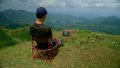 young man watches an old analog television in isolation in the mountains