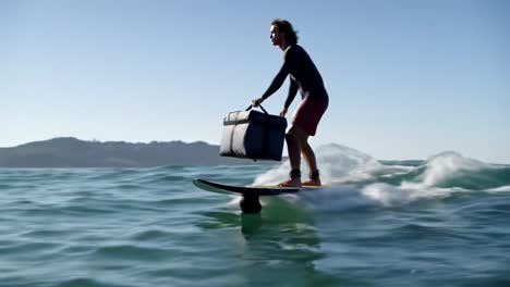 a dynamic experience: man surfing on a foil board while transporting a cooler across the waves towards a yacht under clear blue skies