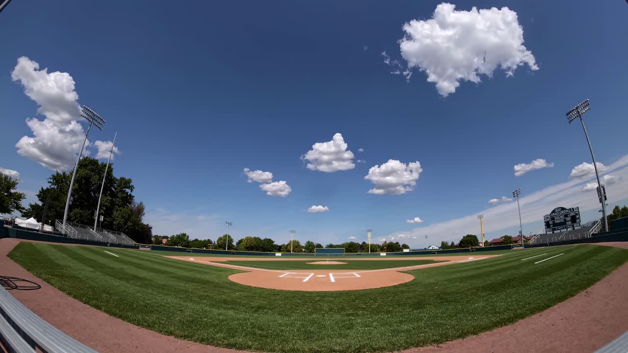 Vista grandangolare di un campo da baseball vuoto sotto un cielo azzurro con nuvole soffici, perfetto