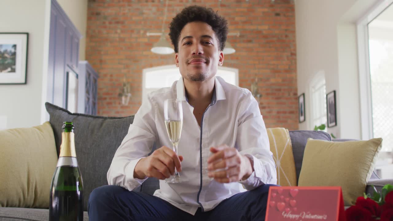 Happy biracial man with champagne making valentine's day video call on laptop