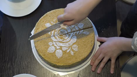 a little girl cuts a beautiful yellow cake that is decorated with a white rose pattern on top. the concept of a home holiday. close-up. top view. faceless. 4k.