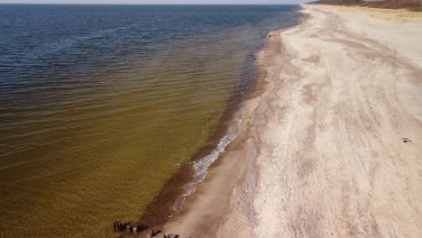 Aerial-view-of-sea-waves-crashing-into-the-beach-with-white-sand-on-a-sunny-spring-day,-Baltic-sea,-Pape-beach,-Latvia,-wide-angle-drone-shot-moving-backwards-camera-tilt-down