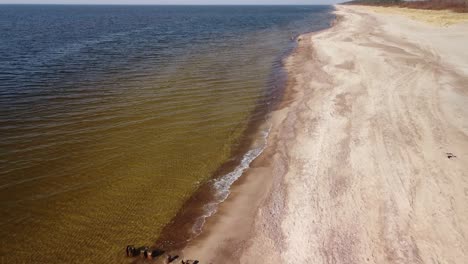 Luftaufnahme-Von-Meereswellen,-Die-An-Einem-Sonnigen-Frühlingstag-In-Den-Strand-Mit-Weißem-Sand-Krachen,-Ostsee,-Pape-Beach,-Lettland,-Weitwinkel-Drohnenaufnahme,-Die-Sich-Rückwärts-Bewegt-Und-Die-Kamera-Nach-Unten-Neigt