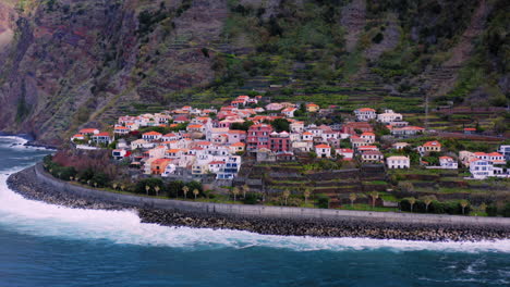 aerial flight towards idyllic portuguese village located in front of gigantic mountain and blue ocean in foreground