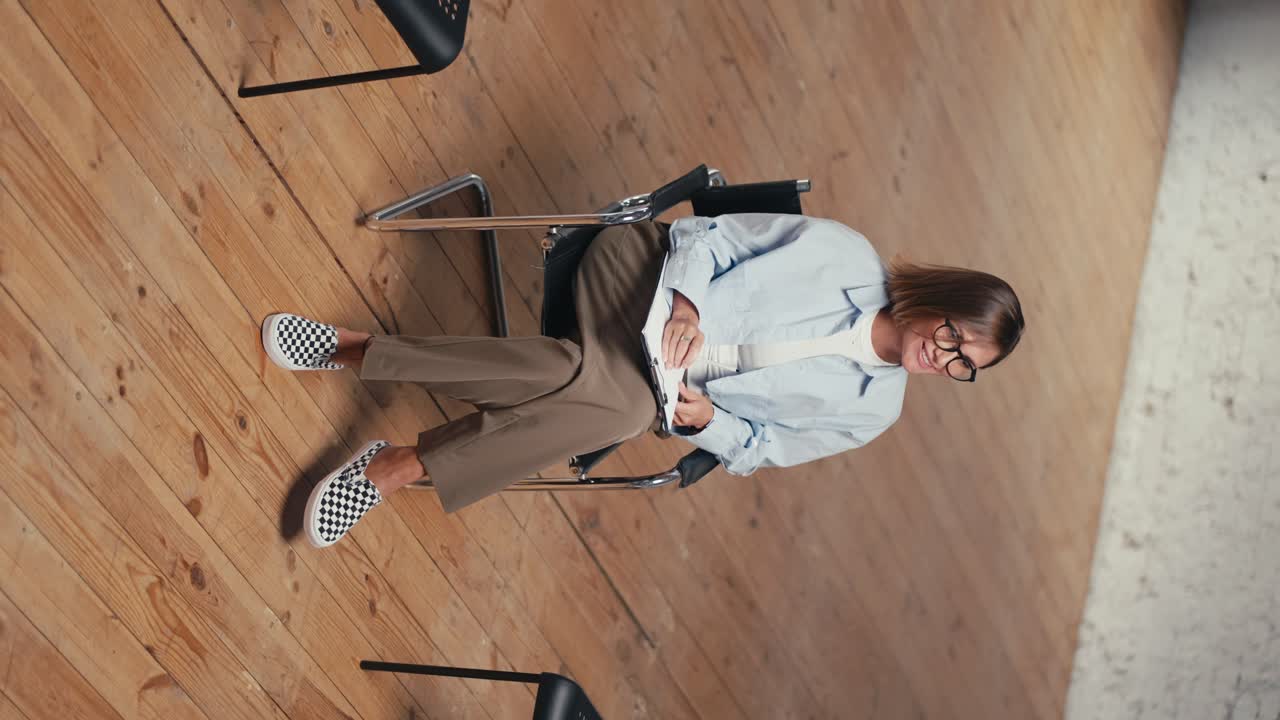 video vertical de una psicóloga con un peinado de bob en gafas en una camisa azul con una tableta y una pluma en sus manos invita a los participantes de la terapia de grupo a tomar sus lugares