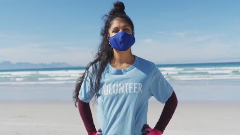 Portrait-of-mixed-race-woman-wearing-volunteer-t-shirt-and-face-mask-looking-at-camera