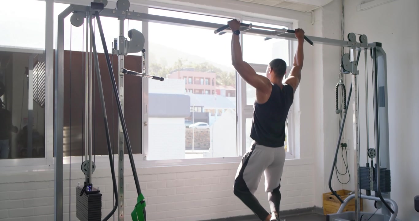 Homem afro-americano de regata entrando na academia, treinando pull-ups com impulso, tocando a janela e olhando para fora.