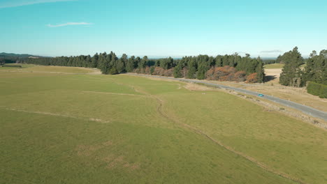 blue car driving through new zealand countryside in canterbury south island drone track in