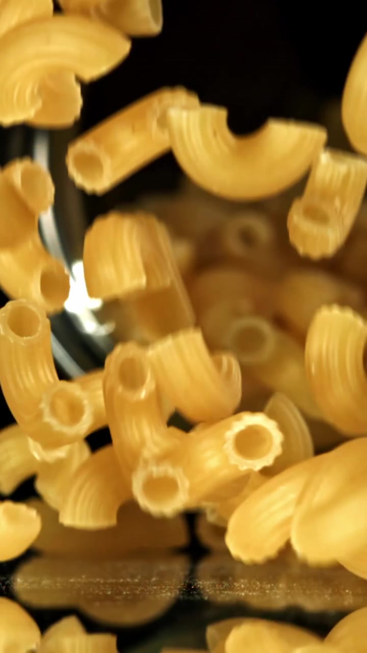 Maccheroni secchi che cadono al rallentatore su una superficie riflettente