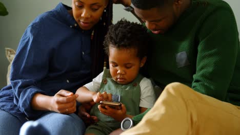 Vista-Frontal-De-Una-Joven-Familia-Negra-Usando-Un-Teléfono-Móvil-Y-Sentada-En-El-Sofá-En-Una-Cómoda-Casa-4k