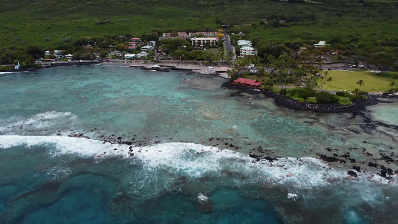 4K cinematic drone zoom-out shot of deep blue water and waves crashing on the beach at Kahalu'u Black Sand Beach in Kona on Hawaii's Big Island
