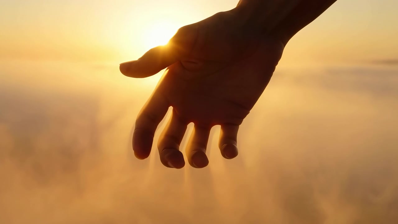Von hinten beleuchtete Hand, die sich während des goldenen Sonnenaufgangs senkt, Finger öffnen sich aus lockerem Griff, während sich die Handfläche zur Kamera dreht, wodurch eine weiche Silhouette, warmes Leuchten, heitere Outdoor-Stimmung und ein sanftes Gefühl entstehen