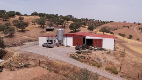 Aerial-orbiting-farm-warehouse-on-countryside-landscape,-arid-fields