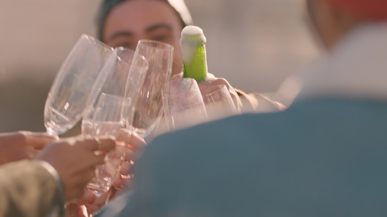 젊은 남자가 샴페인을 터뜨리며 코르크를 터뜨리고 있는 옥상 파티를 축하하는 친구들이 일몰에서 신년 축하를 즐기고 있습니다.