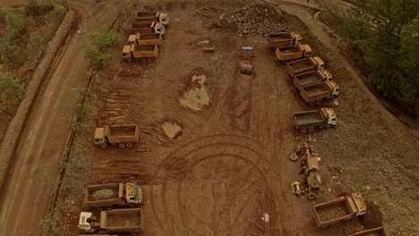 a fleet of dirt covered trucks and diggers parked up side by side in an industrial mining depot