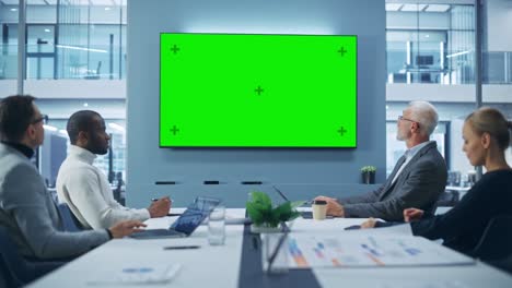 office conference room meeting using video call: multi-ethnic group of top managers, executives talk, use green screen chroma key tv. businesspeople work on an e-commerce strategy. medium wide static