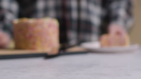 Defocused-Shot-Of-Person-At-Home-Cutting-Slice-From-Rainbow-Celebration-Cake-On-Table-1