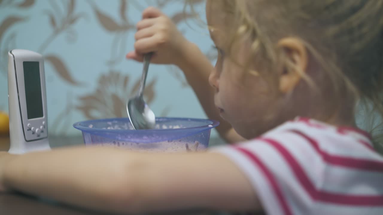 una ragazza divertente mangia pasta al latte controllando il baby monitor nella stanza