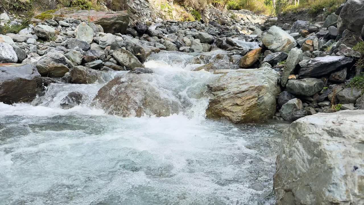 Clear mountain stream rushes over large rocks in a rocky riverbed, captured in daylight with steady camera and natural lighting, creating a dynamic, refreshing mood