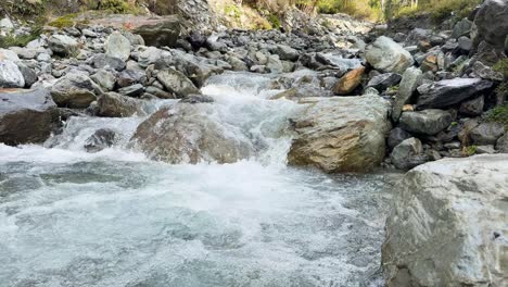 clear mountain stream rushes over large rocks in a rocky riverbed, captured in daylight with steady camera and natural lighting, creating a dynamic, refreshing mood
