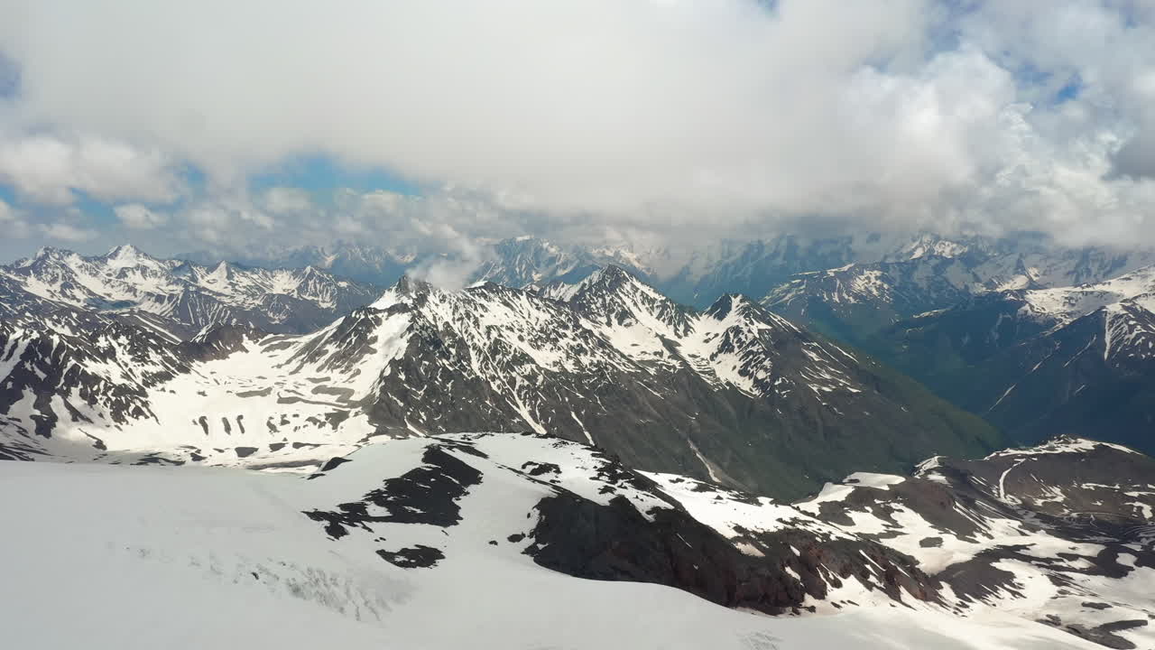 Volo aereo tra le nuvole di montagna sopra splendide vette innevate e ghiacciai.