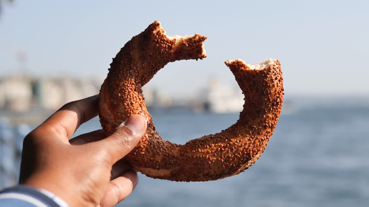 A hand holding a Turkish simit bread with sesame seeds