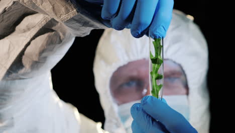 a male scientist holds a flask with a plant