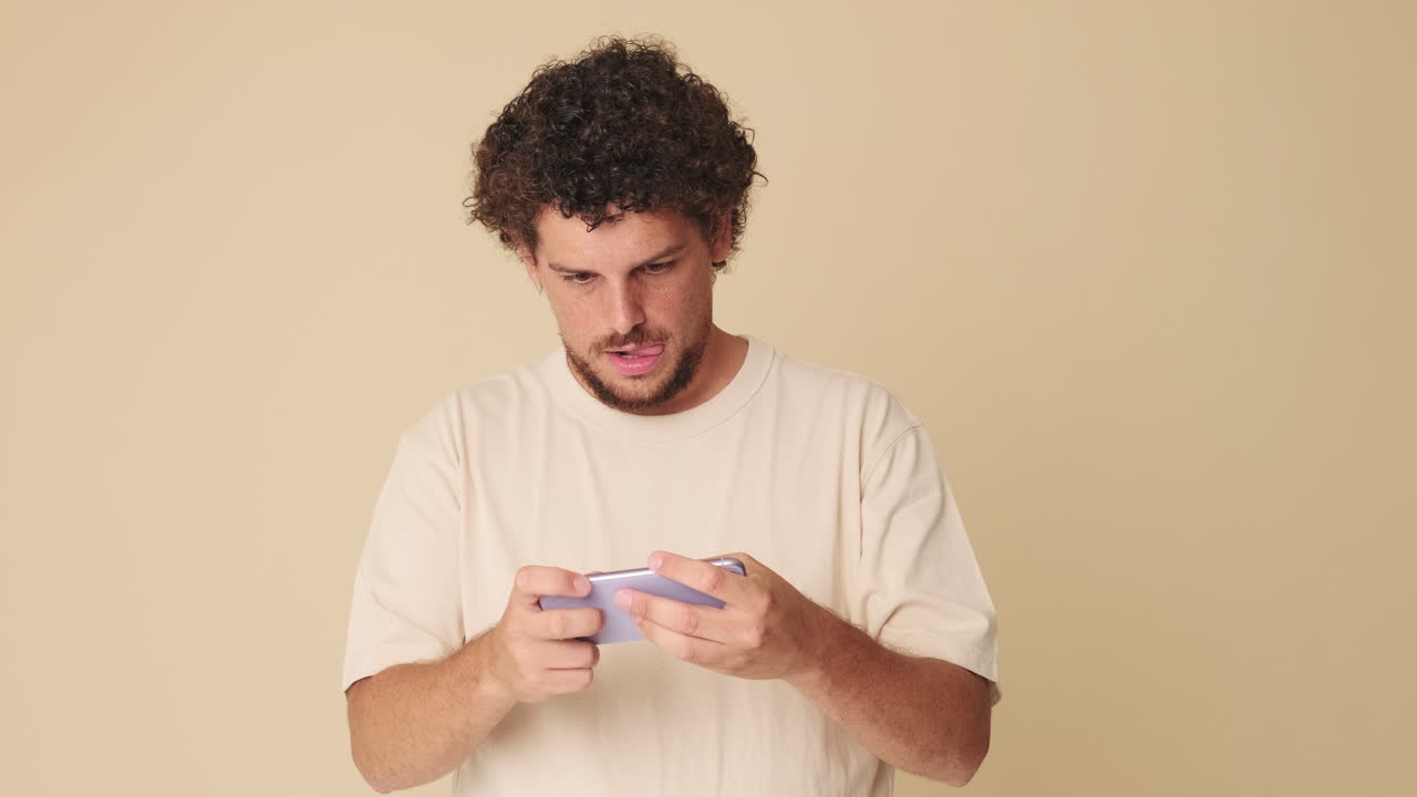 Giovane uomo con capelli ricci che gioca a un videogioco sullo smartphone