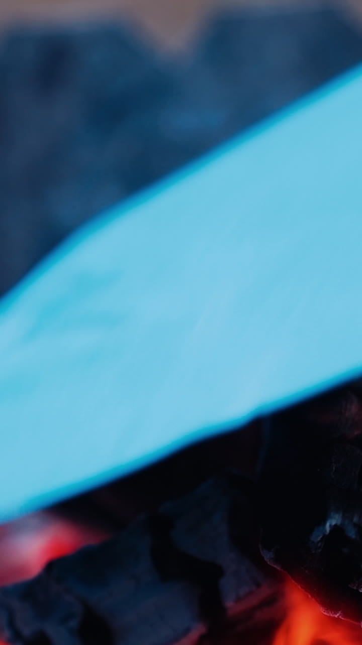 Black charcoal in bonfire close-up. White paper list falling into the fire and burning brightly. Slow motion. Vertical video