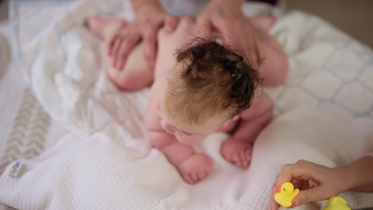 Mulher tentando distrair um bebê chorando deitado em um cobertor durante a massagem com um brinquedo