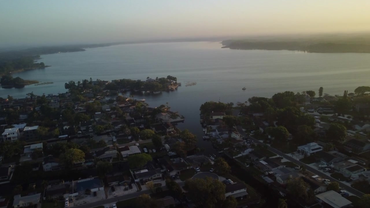 Luftaufnahmen über Palm Harbour und Lake Tarpon bei Sonnenaufgang. Die Drohnenaufnahme beginnt schräg nach unten über Wohngebieten und schwenkt nach oben, während sie sich nach rechts dreht, um den See und den Sonnenaufgang zu zeigen.