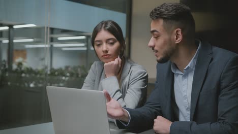 afecto en el trabajo. mujer joven mirando a su apuesto colega árabe y sonriente, hombre ocupado explicando proyecto en la computadora portátil