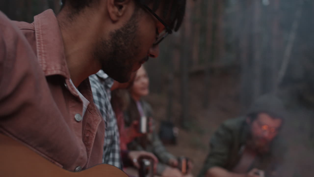 Friends Playing Guitar Around Campfire in Forest