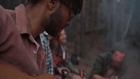 friends playing guitar around campfire in forest
