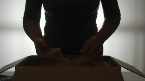 person's hands filling a cardboard box with packing material