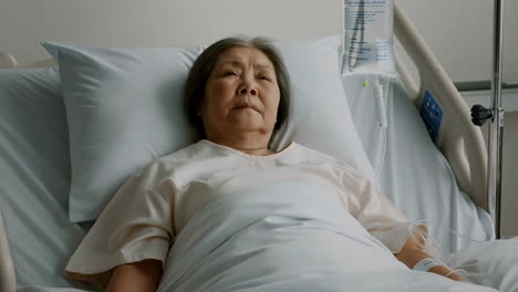 an elderly asian woman lies in a hospital bed with an iv drip