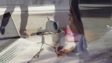 animación de una mujer de negocios biracial grabando usando una computadora portátil sobre personas y paisajes urbanos
