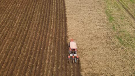 aerial footage capturing a piece of perfectly symmetrical tilled land, with a busy farmer driving a tractor ploughing the farmland, beautiful contrast of soil pattern shown on the ground