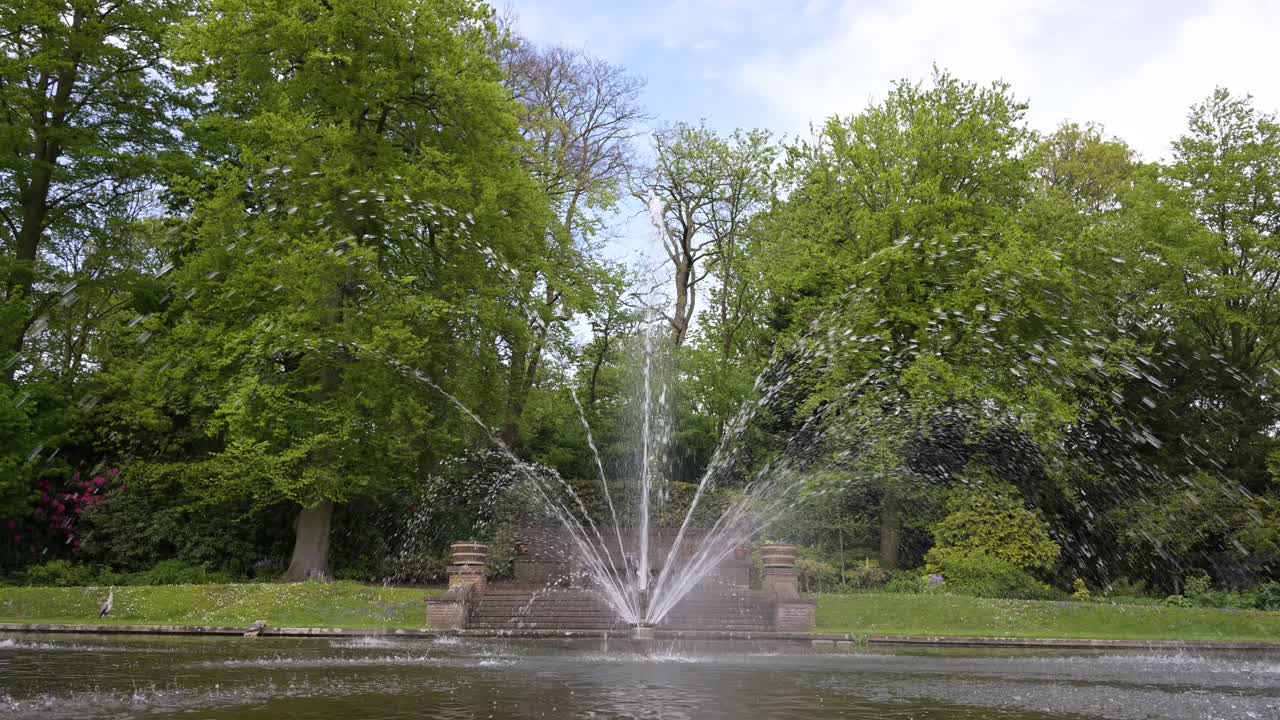 una fuente corriente en el medio de un estanque de agua tranquila bajo un cielo nublado azul durante el tiempo de sprint temprano