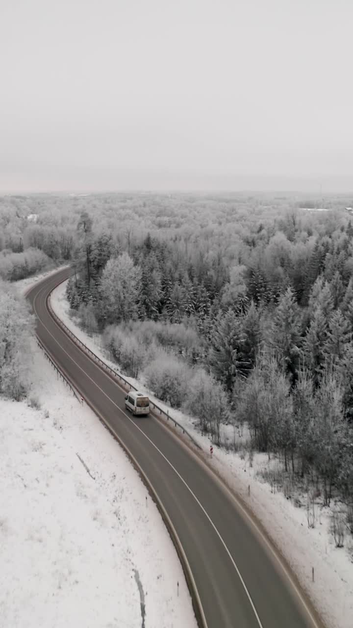 Vertical drone view of a car driving on a winding highway road through a frozen winter forest landscape with icy trees. Vehicle in a winter wonderland scenery. Frost on the trees after extreme cold.