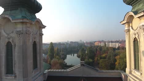 aerial shot as flying through between church bell towers, revealing a park with a lake